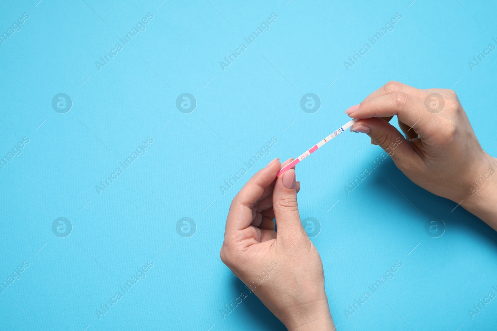 Photo of Woman holding pregnancy test on light blue background, above view. Space for text