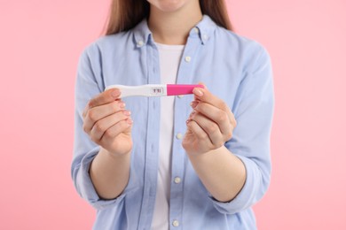 Photo of Woman holding pregnancy test on pink background, closeup