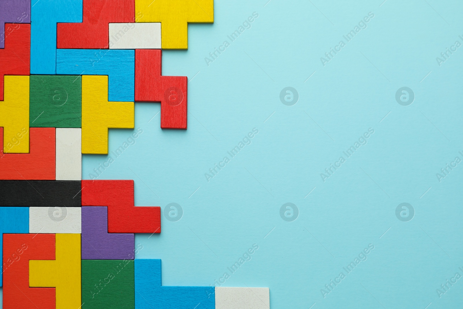 Photo of Colorful wooden puzzle pieces on light blue background, top view. Space for text