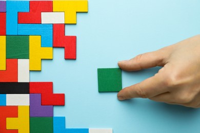 Photo of Woman playing with colorful wooden puzzle pieces on light blue background, top view