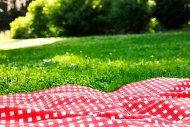 Checkered picnic tablecloth on green grass, closeup. Space for text