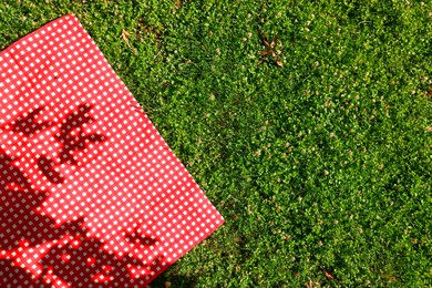 Checkered picnic tablecloth on green grass, top view. Space for text