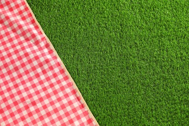 Photo of Checkered picnic tablecloth on green grass, top view. Space for text