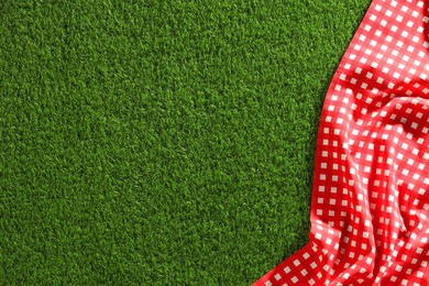 Checkered picnic tablecloth on green grass, top view. Space for text