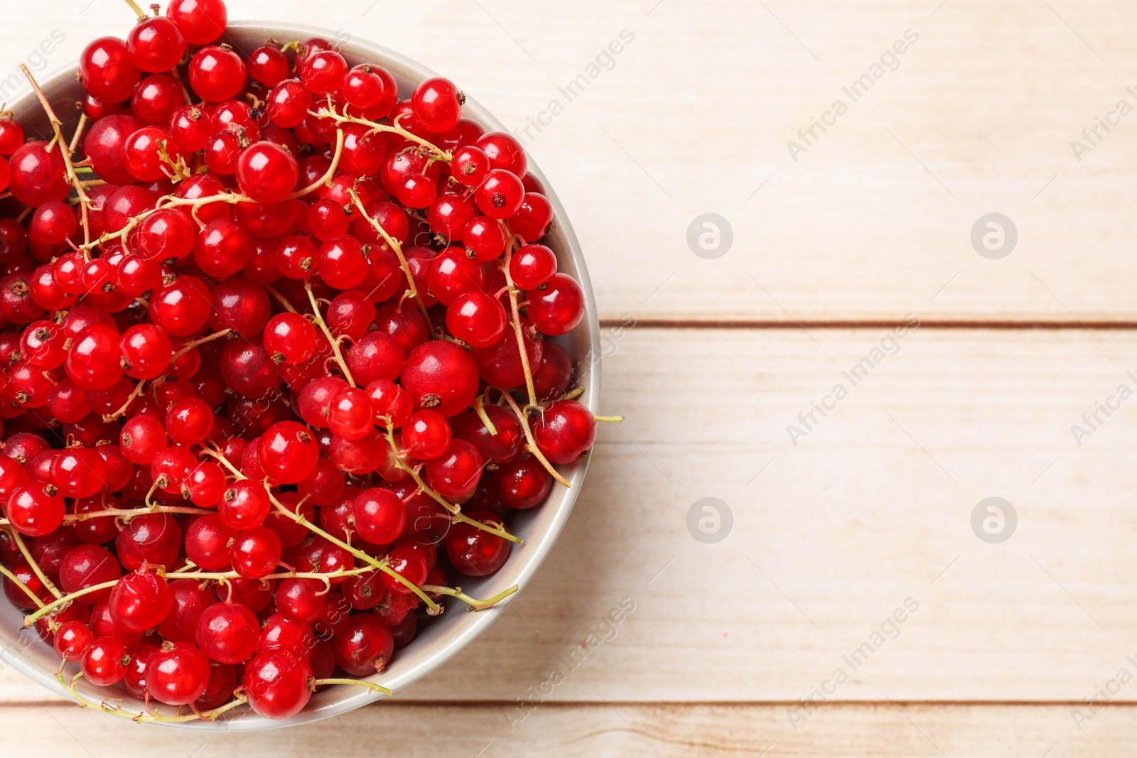 Photo of Fresh red currant berries in bowl on white wooden table, top view. Space for text