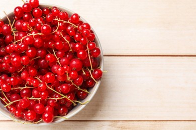 Photo of Fresh red currant berries in bowl on white wooden table, top view. Space for text