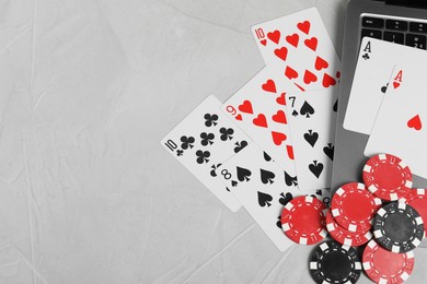 Photo of Online poker. Playing cards, chips and laptop on light grey table, top view. Space for text