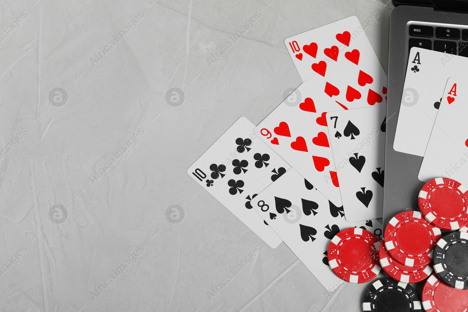 Photo of Online poker. Playing cards, chips and laptop on light grey table, top view. Space for text