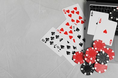 Photo of Online poker. Playing cards, chips and laptop on light grey table, top view. Space for text