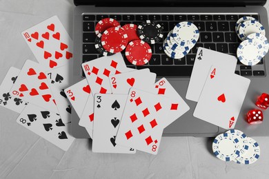 Photo of Online poker. Playing cards, chips, dice and laptop on light grey table, top view