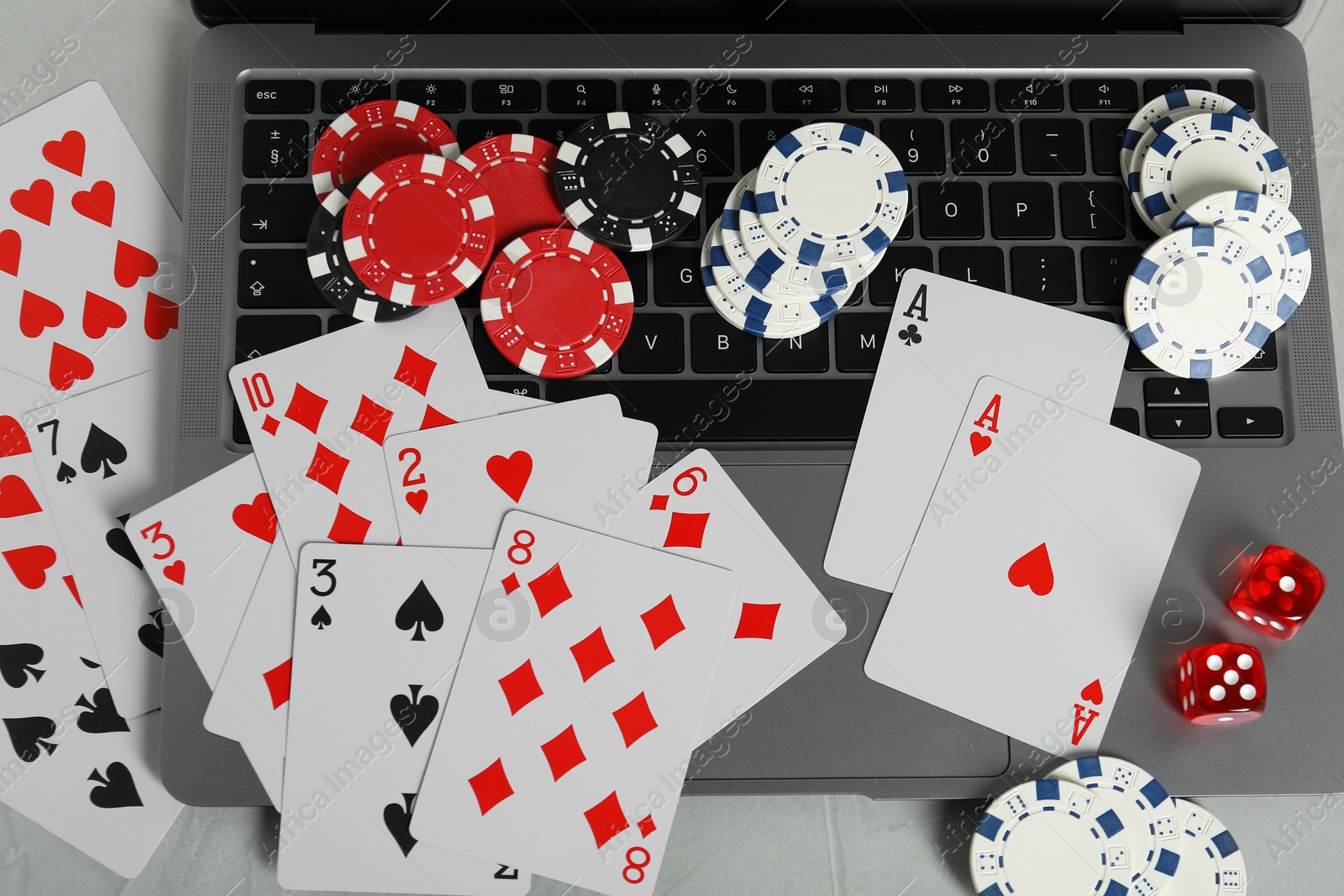 Photo of Online poker. Playing cards, chips, dice and laptop on light grey table, top view