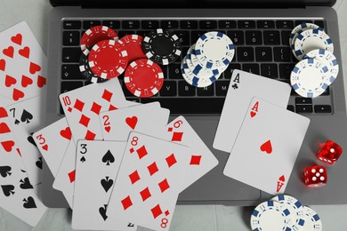 Photo of Online poker. Playing cards, chips, dice and laptop on light grey table, top view