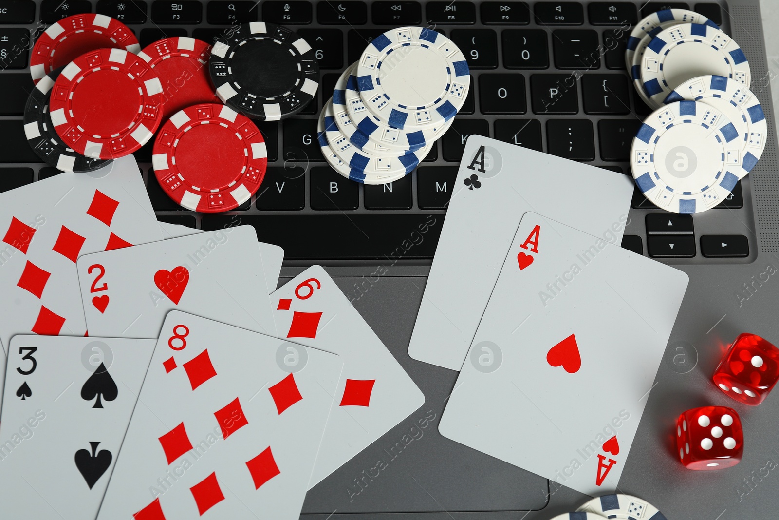 Photo of Online poker. Playing cards, dice and chips on laptop, top view