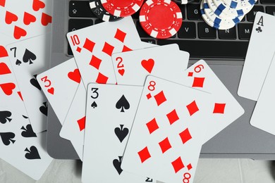 Photo of Online poker. Playing cards, chips and laptop on light grey table, top view