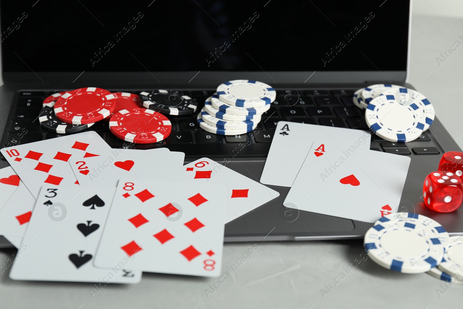 Photo of Online poker. Playing cards, chips, dice and laptop on light grey table