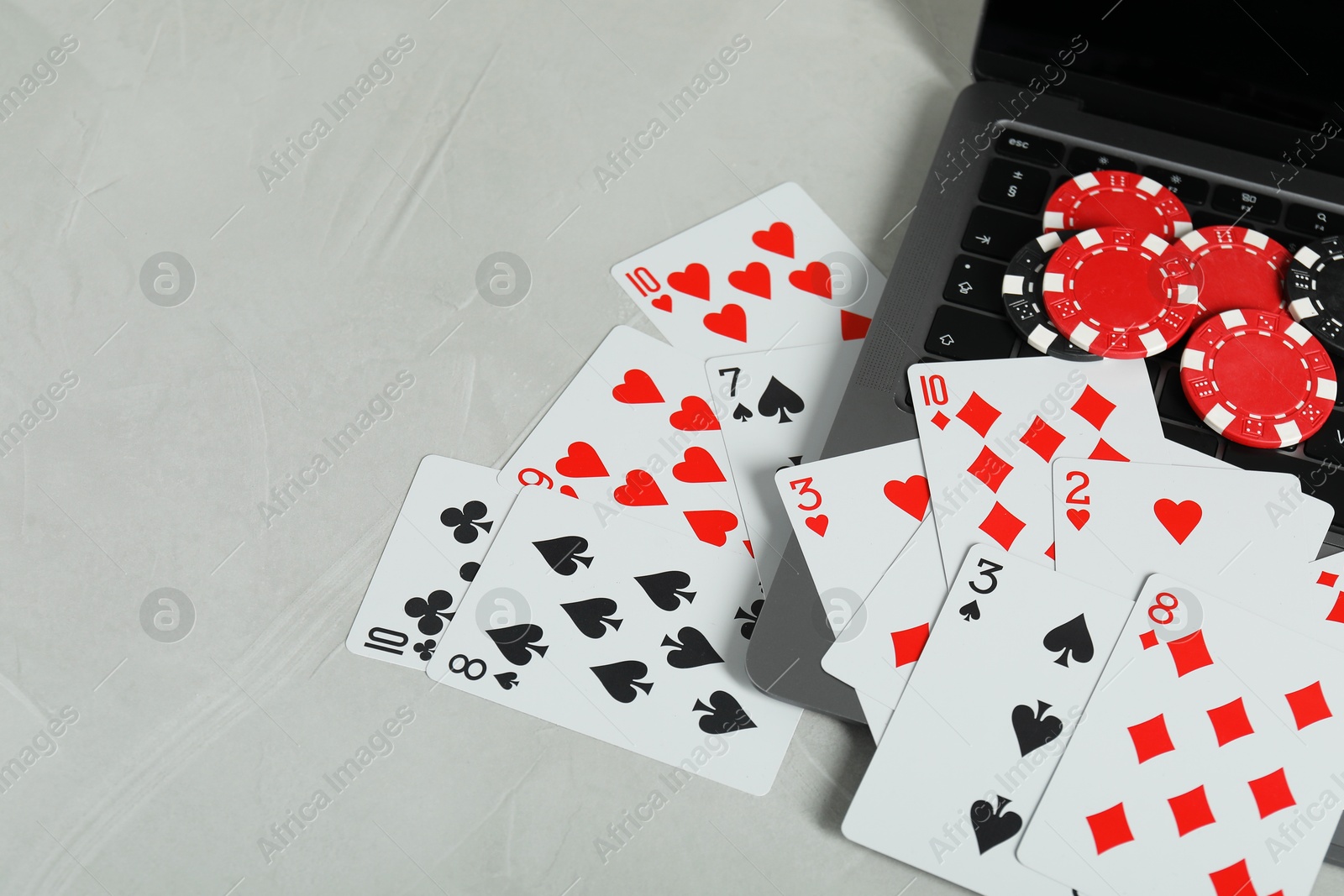 Photo of Online poker. Playing cards, chips and laptop on light grey table, space for text