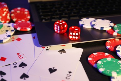 Photo of Online poker. Playing cards, chips, dice and laptop on black table, closeup