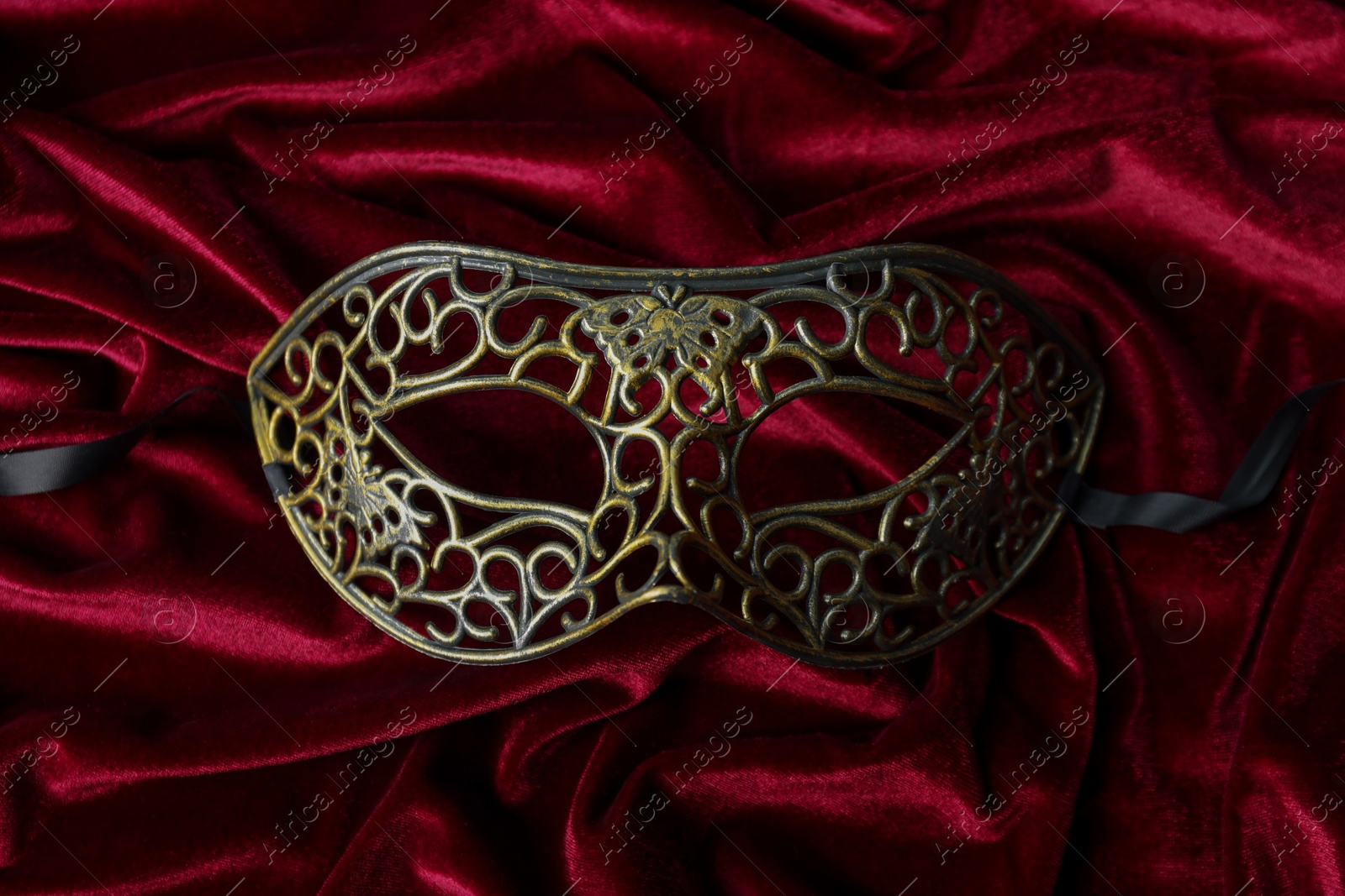 Photo of One beautiful carnival mask on red fabric, top view