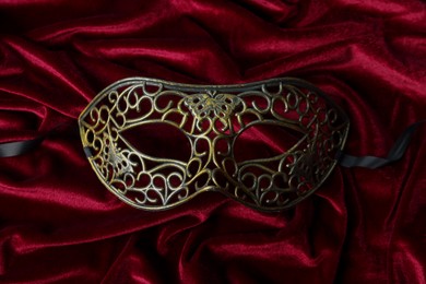 Photo of One beautiful carnival mask on red fabric, top view