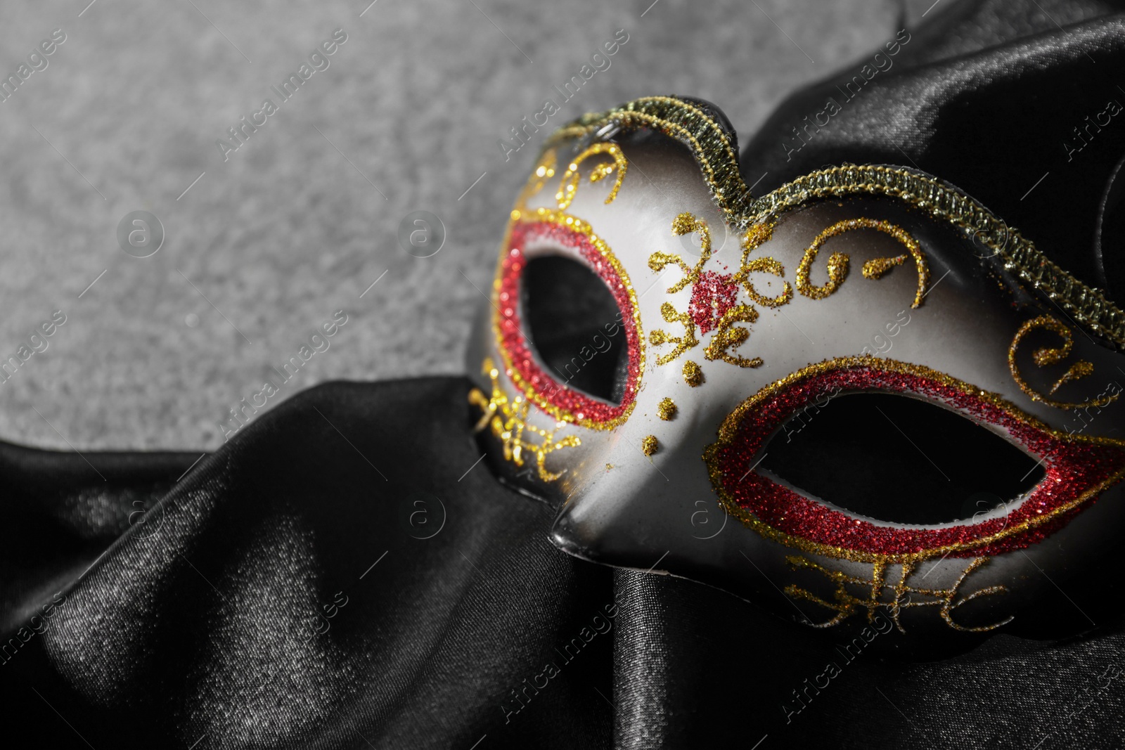 Photo of Beautiful carnival mask and black fabric on grey table