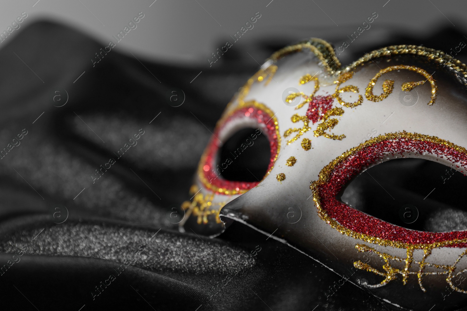 Photo of One beautiful carnival mask on black fabric, closeup. Space for text