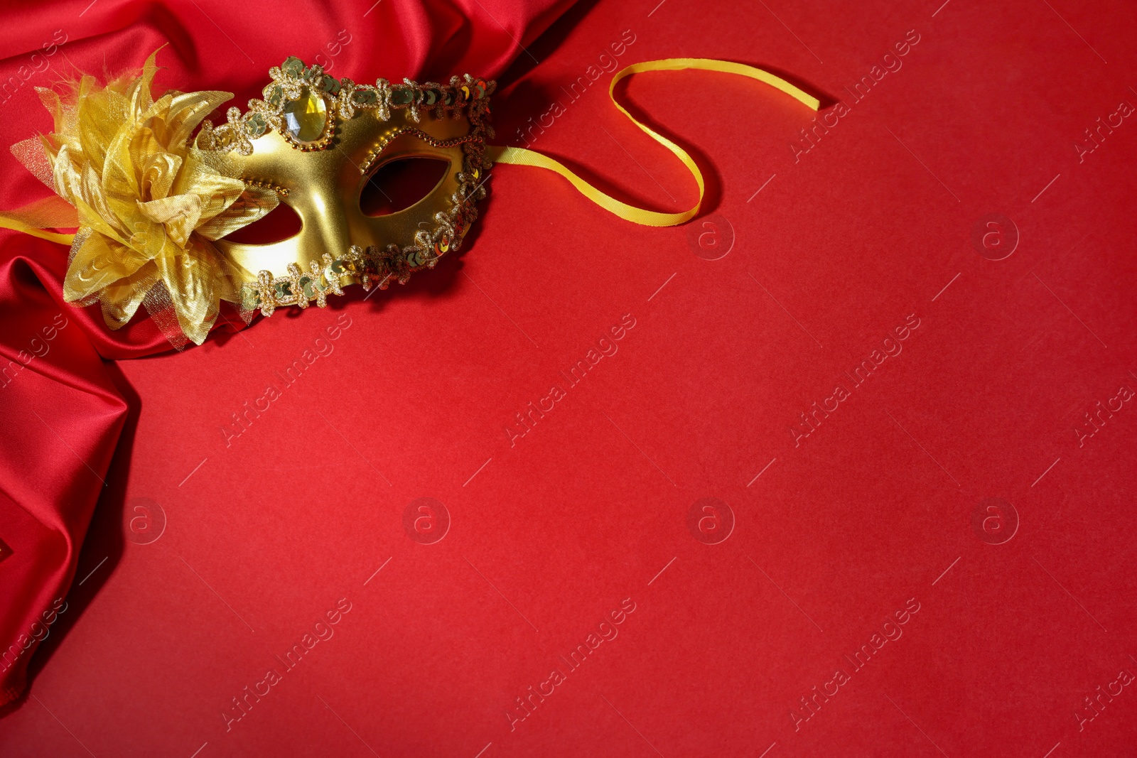 Photo of Beautiful carnival mask and fabric on red background, space for text