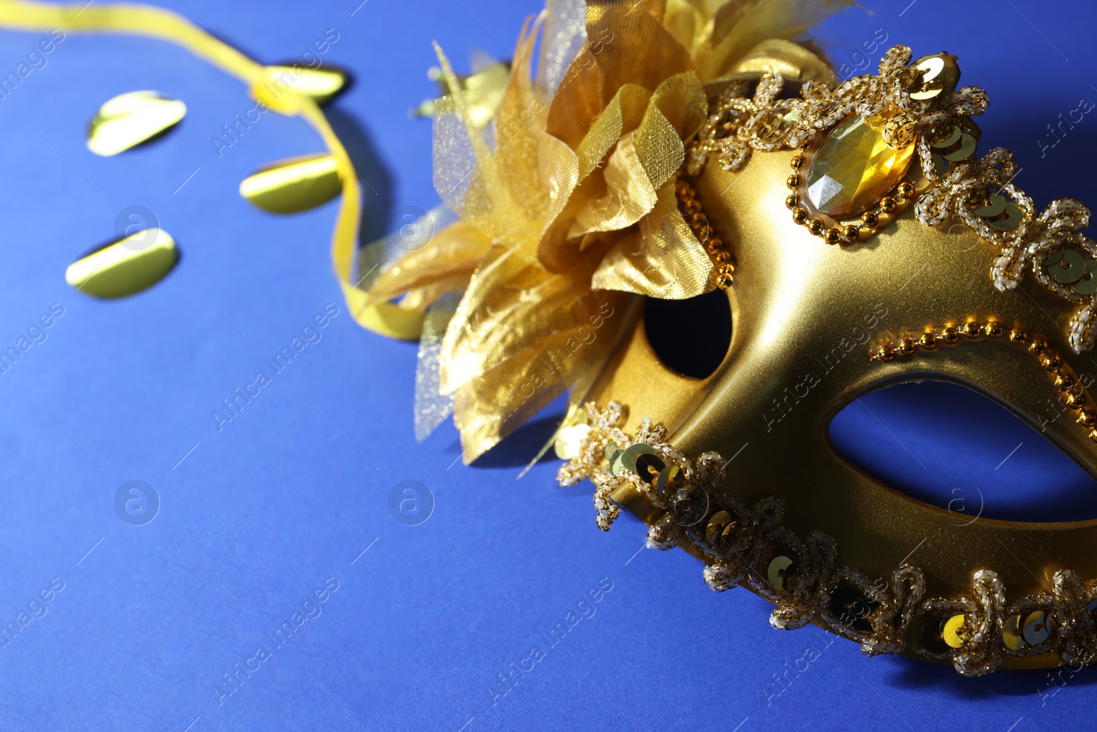 Photo of Beautiful carnival mask and confetti on blue background, closeup