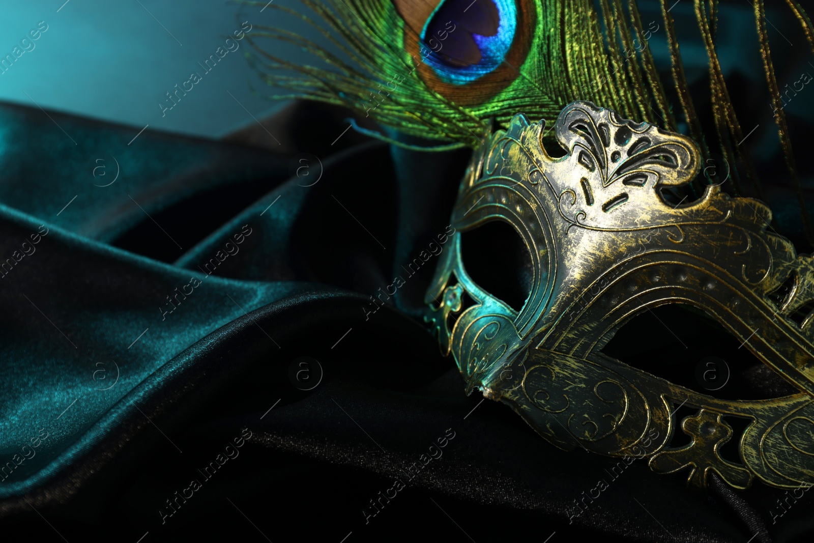 Photo of Beautiful carnival mask and peacock feather on black fabric, closeup. Space for text