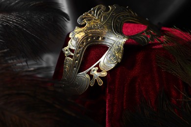 Photo of Beautiful carnival mask and peacock feathers on red fabric, closeup