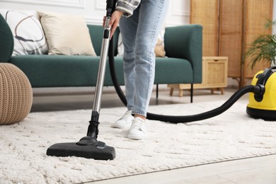 Woman cleaning carpet with vacuum in living room, closeup