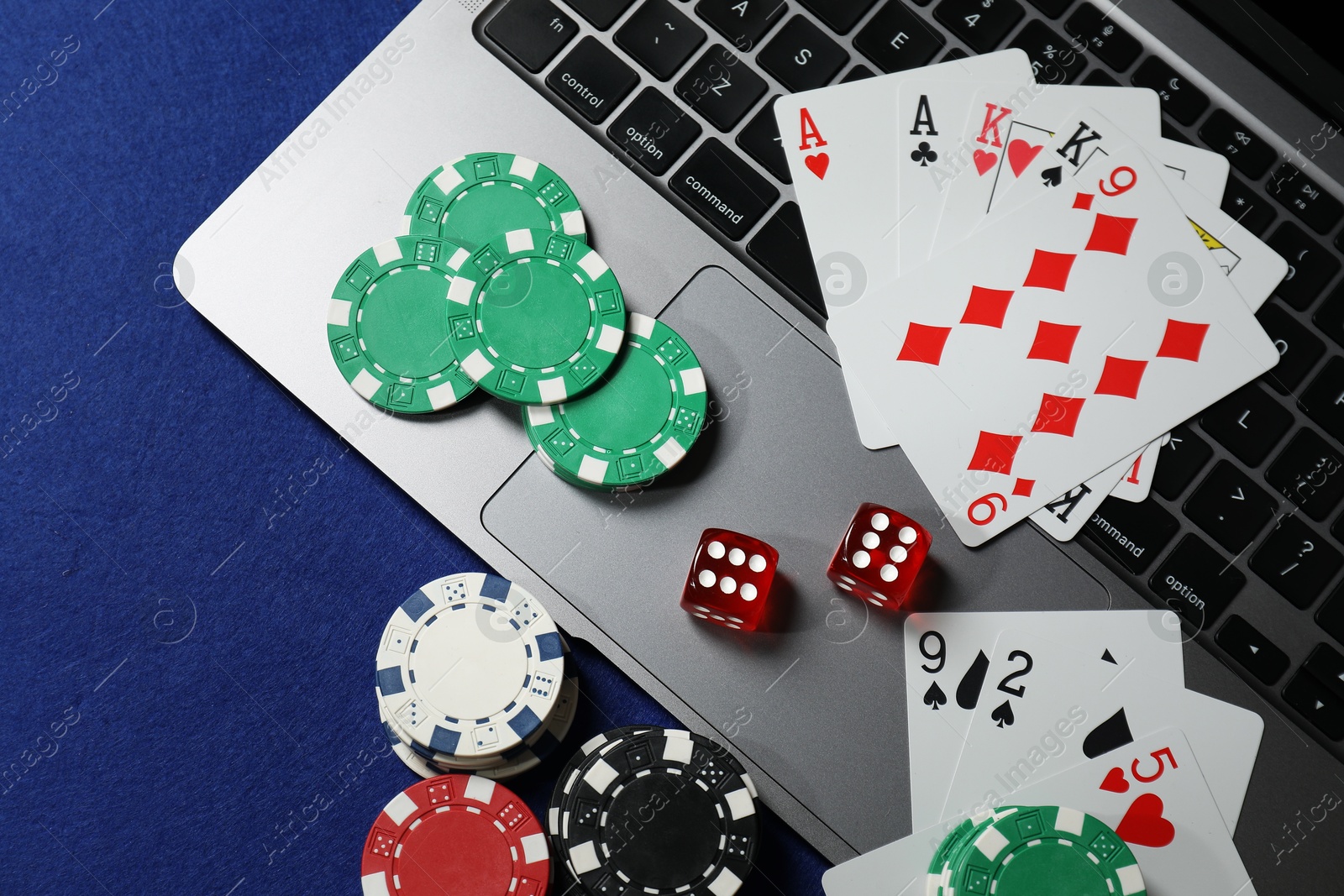 Photo of Poker chips, laptop, playing cards and dices on blue table, flat lay. Online game