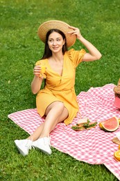 Smiling woman with glass of juice having picnic on green grass