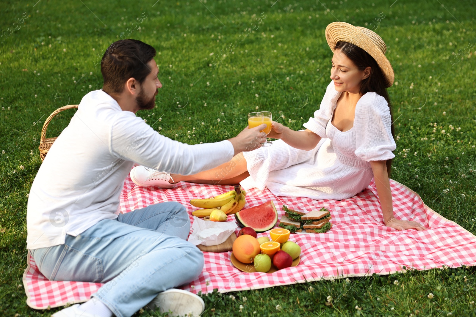 Photo of Lovely couple clinking glasses of juice on picnic blanket outdoors