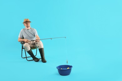 Fisherman with rod having fun against light blue background