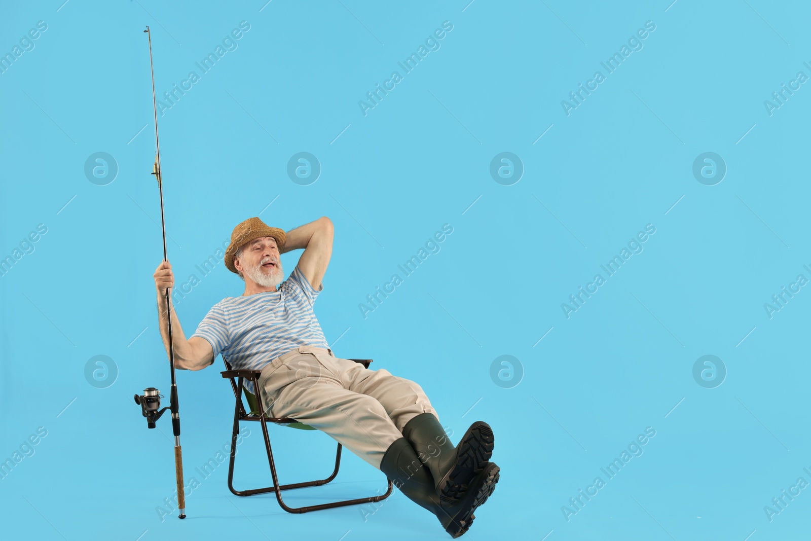 Photo of Fisherman with rod on fishing chair against light blue background. Space for text