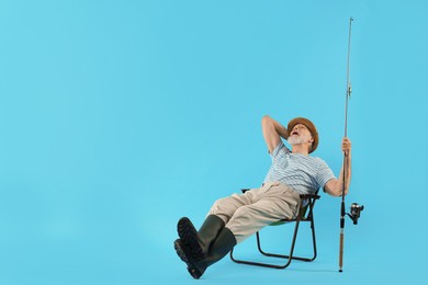 Photo of Fisherman with rod on fishing chair against light blue background. Space for text