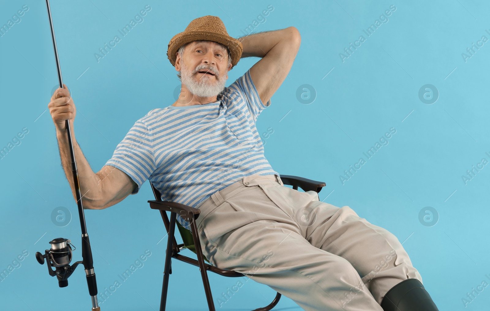 Photo of Fisherman with rod on fishing chair against light blue background