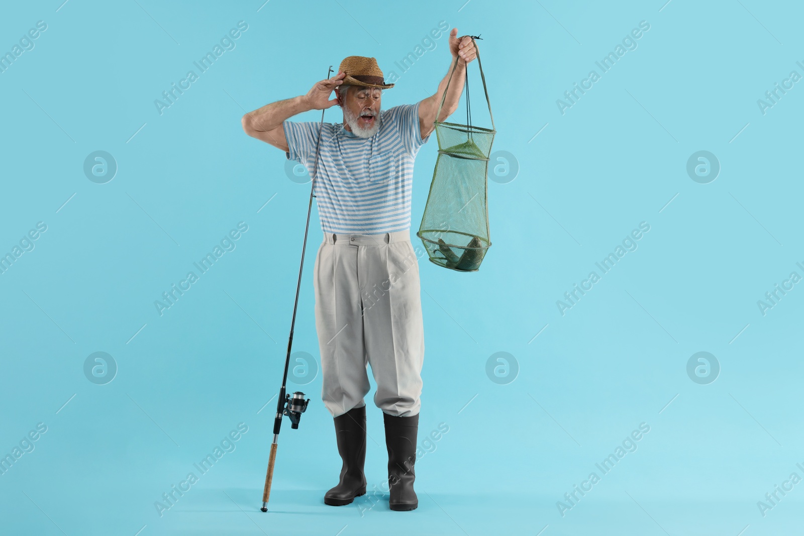 Photo of Fisherman holding rod and fishing net with catch on light blue background