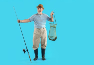 Fisherman holding rod and fishing net with catch on light blue background