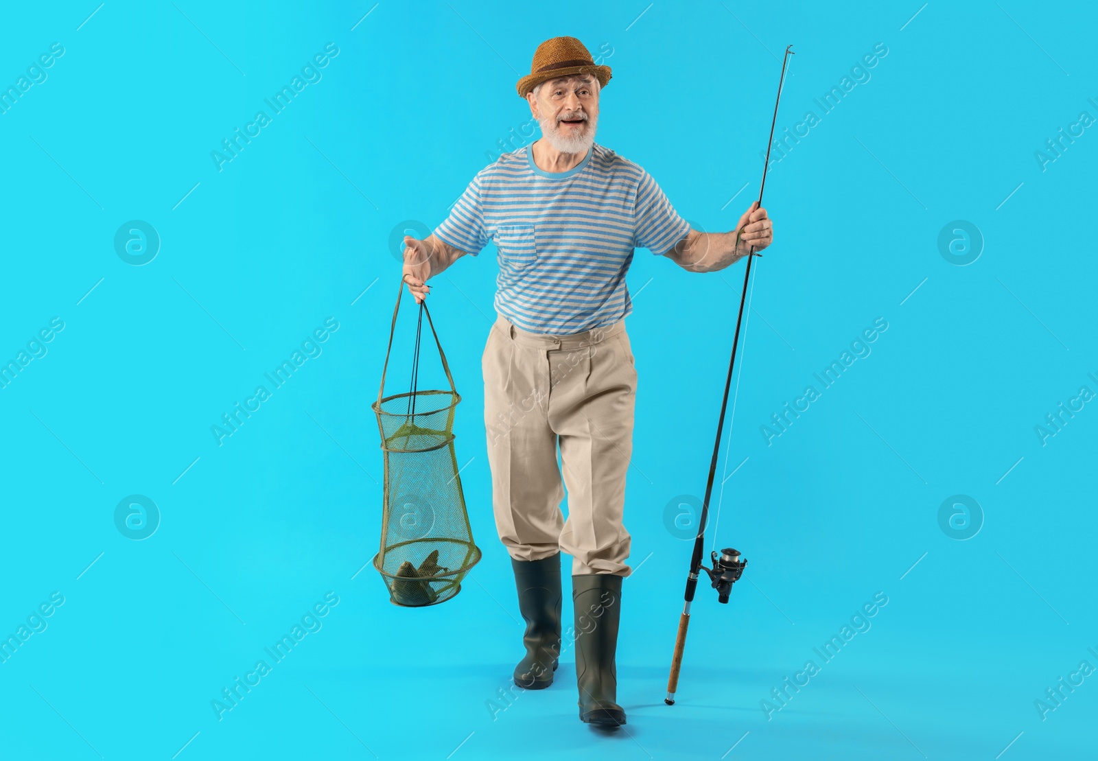 Photo of Fisherman holding rod and fishing net with catch on light blue background