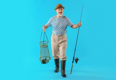 Fisherman holding rod and fishing net with catch on light blue background