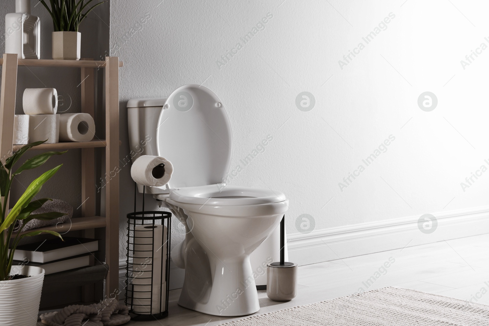 Photo of White toilet bowl, paper rolls and houseplants in bathroom. Space for text