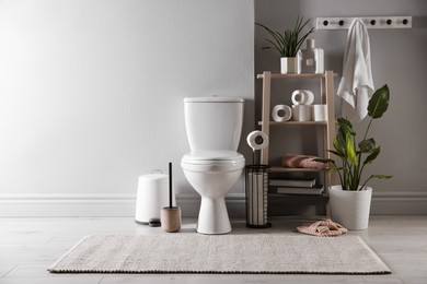 Photo of White toilet bowl, paper rolls and houseplants in bathroom