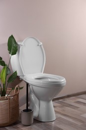 Photo of White toilet bowl and houseplant near beige wall indoors