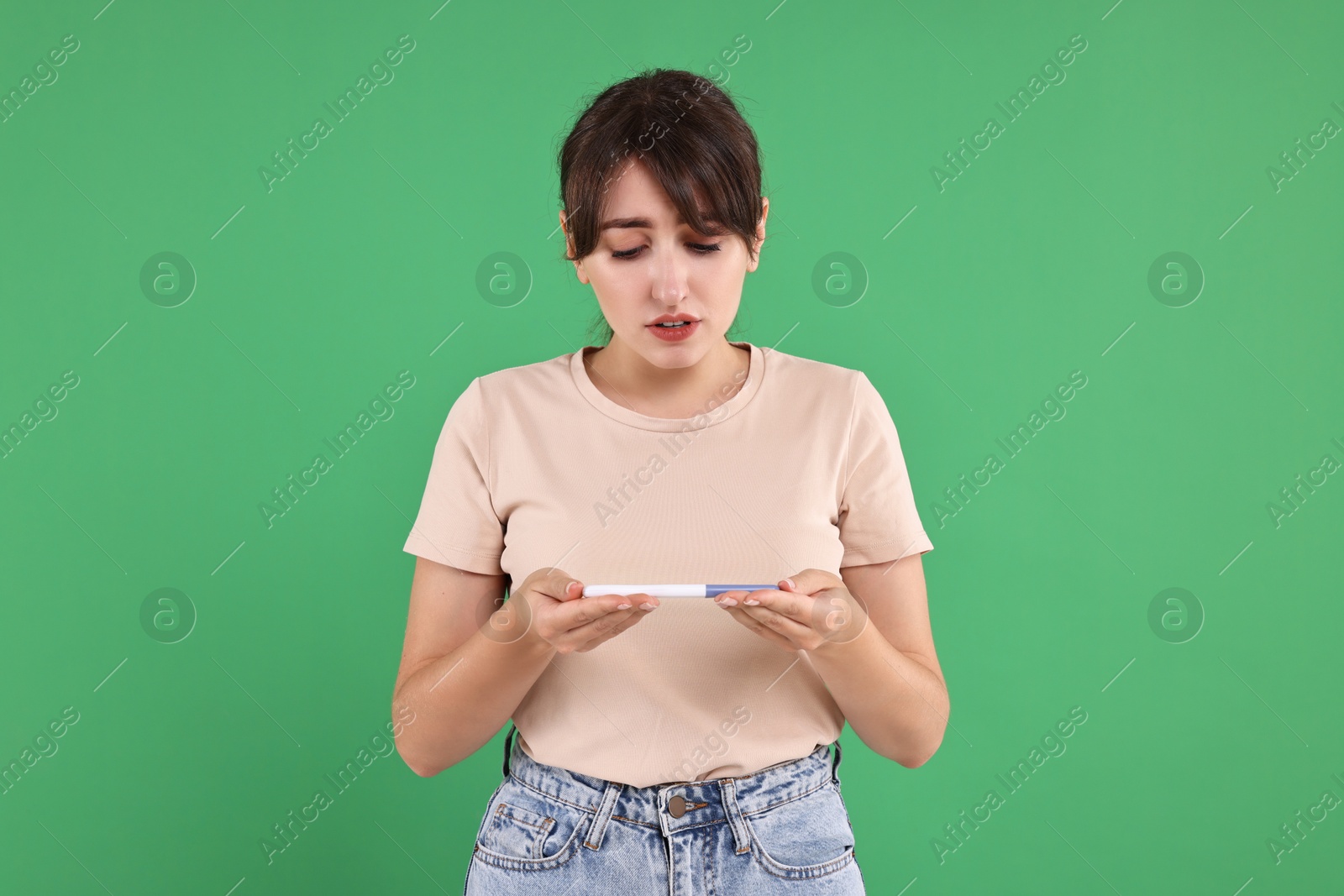 Photo of Worried young woman with pregnancy test on green background