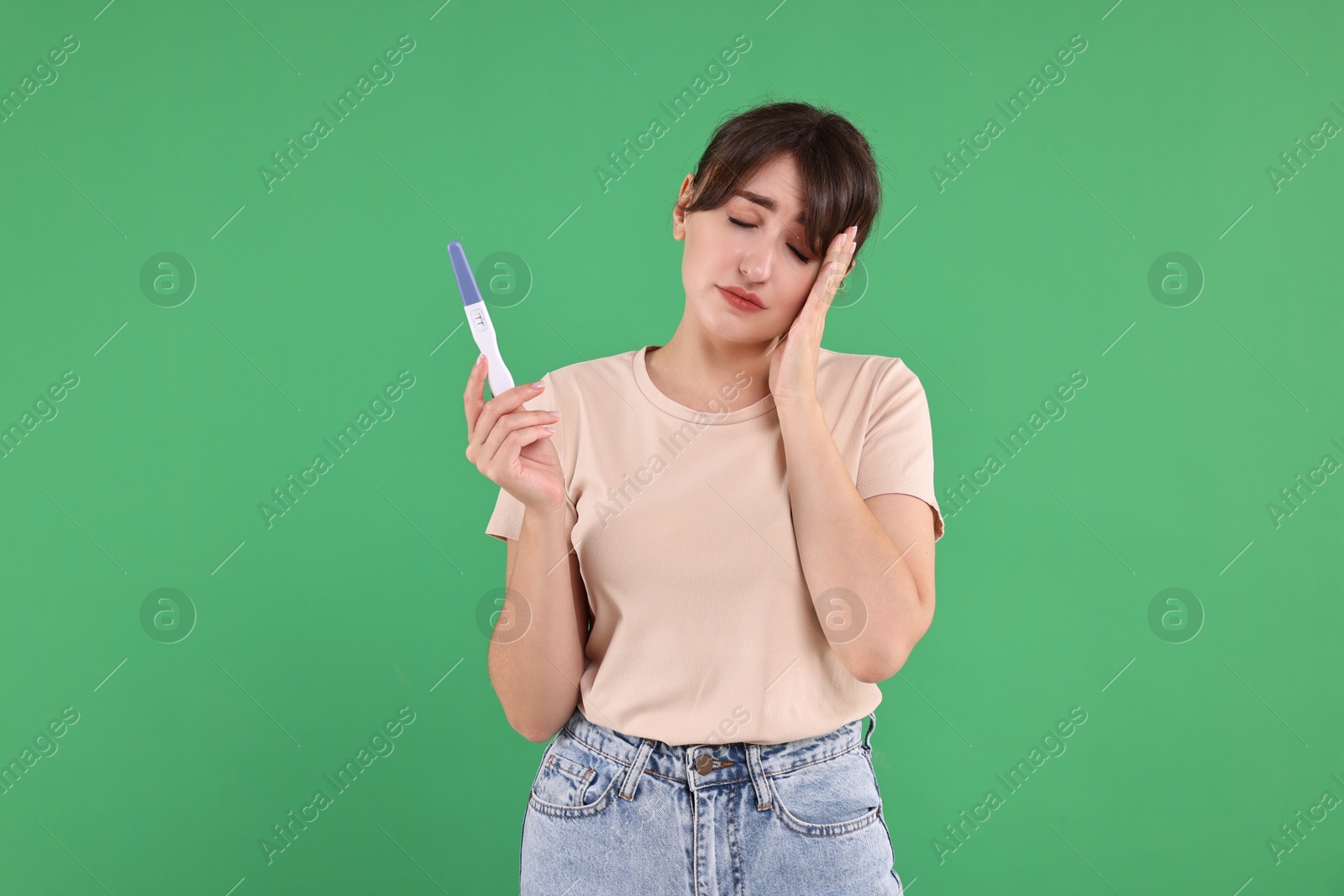 Photo of Worried young woman with pregnancy test on green background