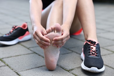 Photo of Woman suffering from foot pain outdoors, closeup