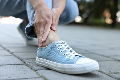 Photo of Woman suffering from foot pain outdoors, closeup