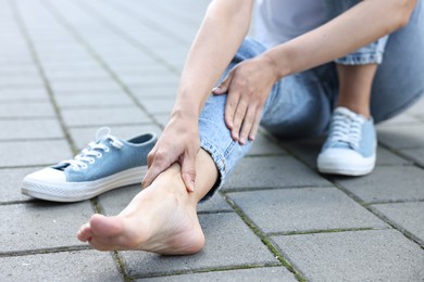 Photo of Woman suffering from foot pain outdoors, closeup