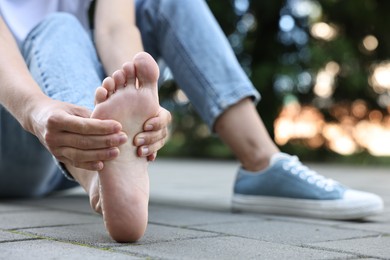 Photo of Woman suffering from foot pain outdoors, closeup